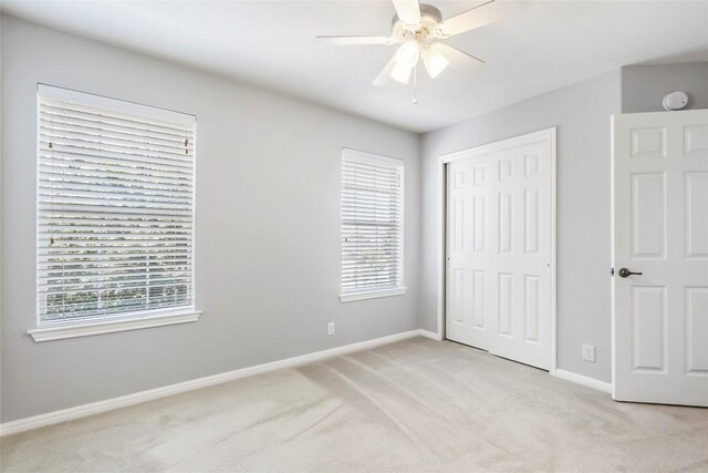 unfurnished bedroom featuring ceiling fan, light colored carpet, a closet, and multiple windows