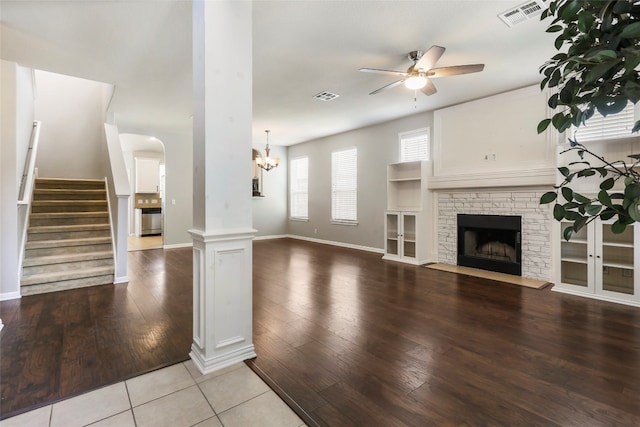 unfurnished living room featuring light hardwood / wood-style flooring, decorative columns, ceiling fan with notable chandelier, and a fireplace