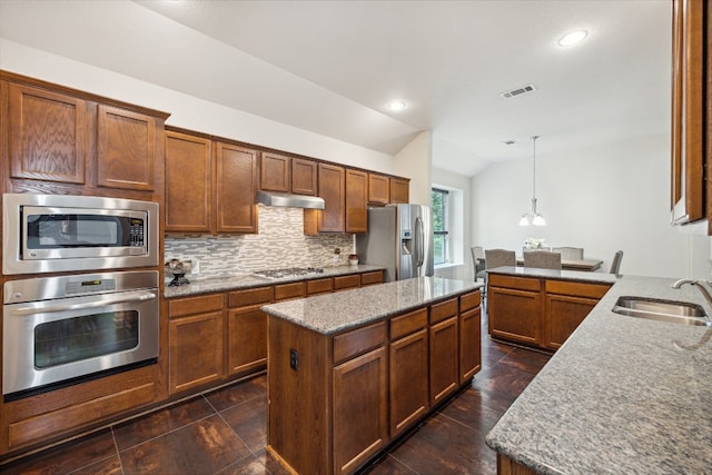 kitchen featuring vaulted ceiling, a kitchen island, decorative light fixtures, sink, and stainless steel appliances