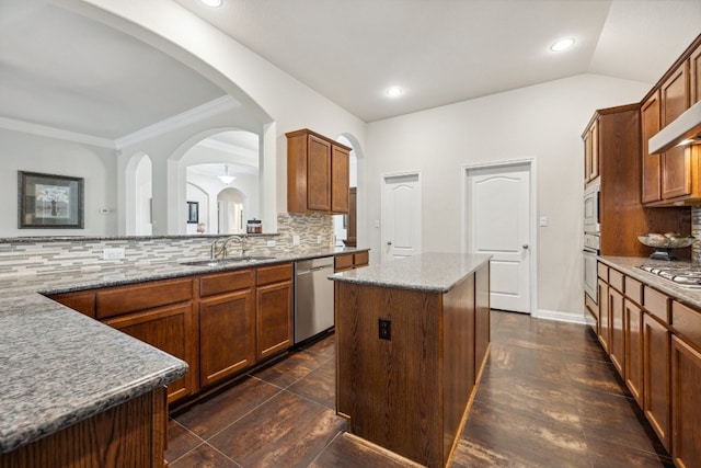 kitchen featuring sink, light stone counters, a center island, appliances with stainless steel finishes, and backsplash