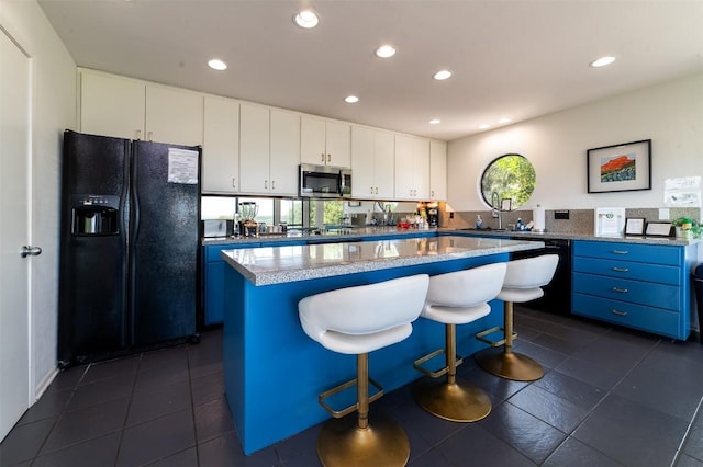 kitchen with light stone countertops, a kitchen island, a kitchen bar, white cabinets, and black appliances