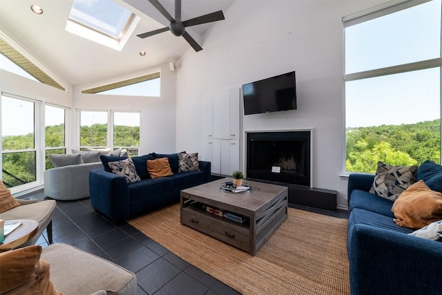 living room featuring dark tile patterned flooring, ceiling fan, high vaulted ceiling, and a skylight