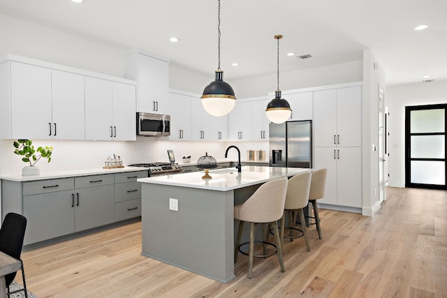 kitchen with gray cabinetry, hanging light fixtures, appliances with stainless steel finishes, white cabinets, and light wood-type flooring