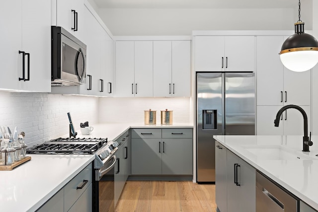 kitchen with sink, gray cabinets, light wood-type flooring, appliances with stainless steel finishes, and decorative light fixtures