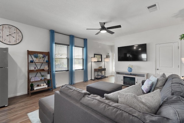 living room featuring ceiling fan, light hardwood / wood-style floors, and a textured ceiling