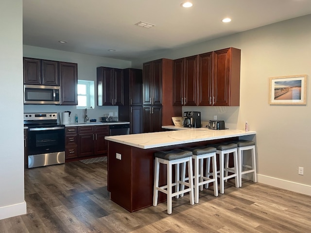 kitchen with stainless steel appliances, kitchen peninsula, a kitchen bar, and wood-type flooring