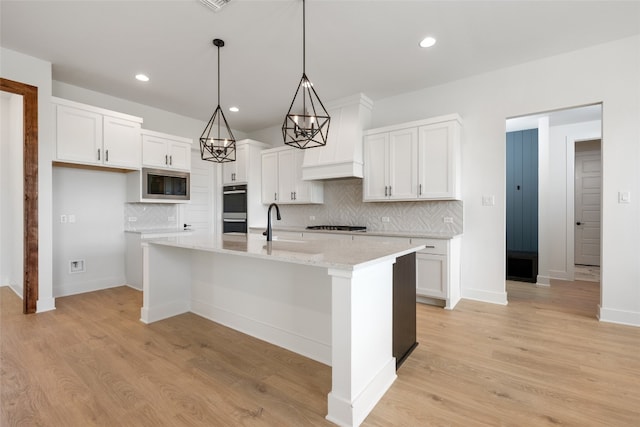 kitchen featuring appliances with stainless steel finishes, decorative backsplash, light hardwood / wood-style floors, white cabinetry, and a center island with sink