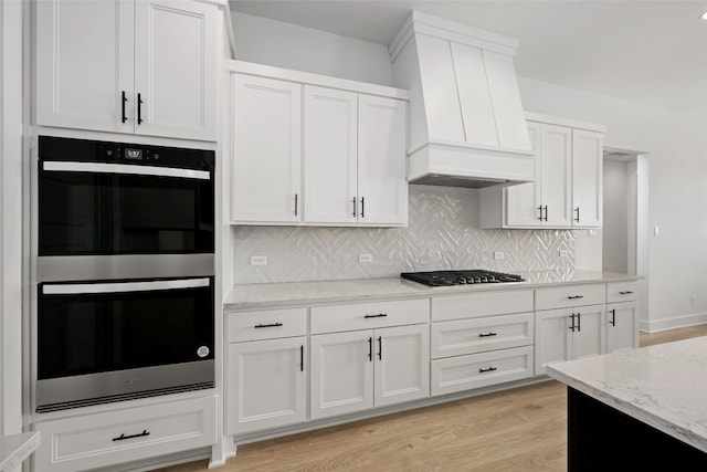 kitchen featuring backsplash, custom range hood, white cabinetry, light hardwood / wood-style floors, and stainless steel appliances