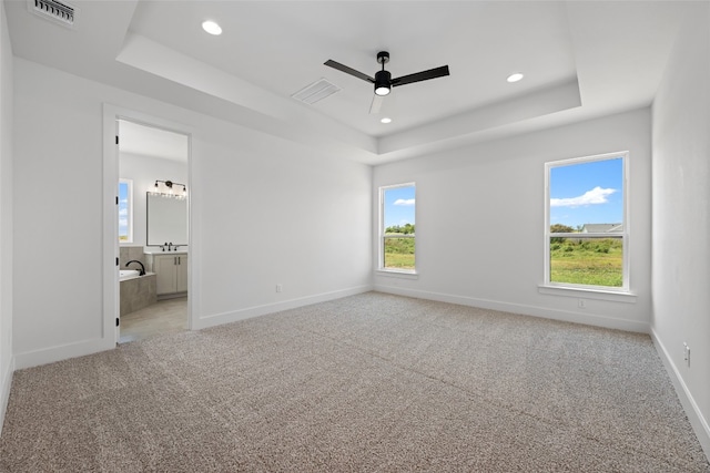 unfurnished bedroom featuring ceiling fan, light carpet, a raised ceiling, and ensuite bath