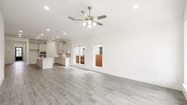 unfurnished living room with a wealth of natural light, ceiling fan, and light wood-type flooring