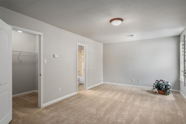 unfurnished bedroom with ensuite bath, a spacious closet, a closet, and light carpet