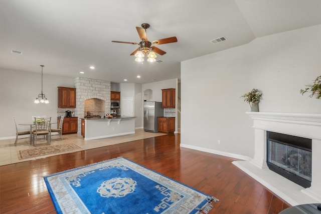 unfurnished living room featuring a large fireplace, dark wood-type flooring, and ceiling fan with notable chandelier