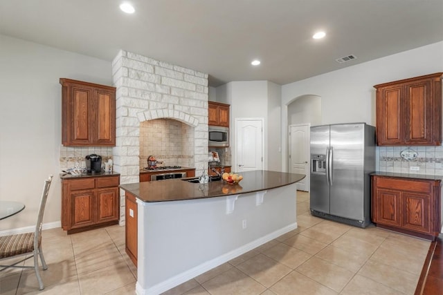 kitchen featuring backsplash, a kitchen island with sink, light tile patterned floors, and stainless steel appliances