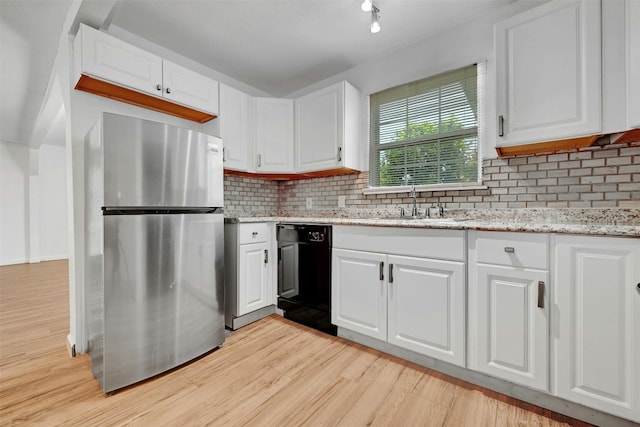 kitchen featuring stainless steel refrigerator, dishwasher, white cabinetry, light stone countertops, and light wood-type flooring