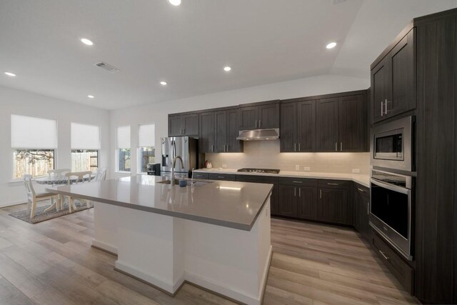 kitchen with an island with sink, sink, backsplash, stainless steel appliances, and lofted ceiling