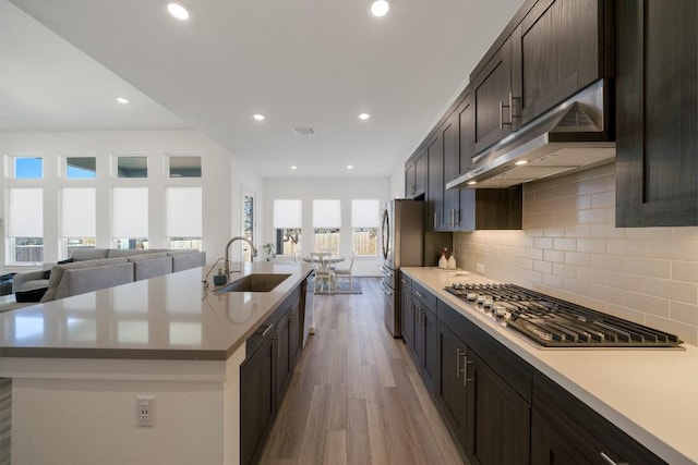 kitchen with stainless steel appliances, an island with sink, light hardwood / wood-style floors, sink, and decorative backsplash