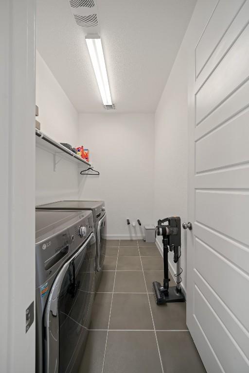 laundry area featuring dark tile patterned flooring, a textured ceiling, and washing machine and clothes dryer