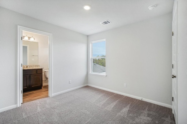 unfurnished bedroom with ensuite bath and light colored carpet