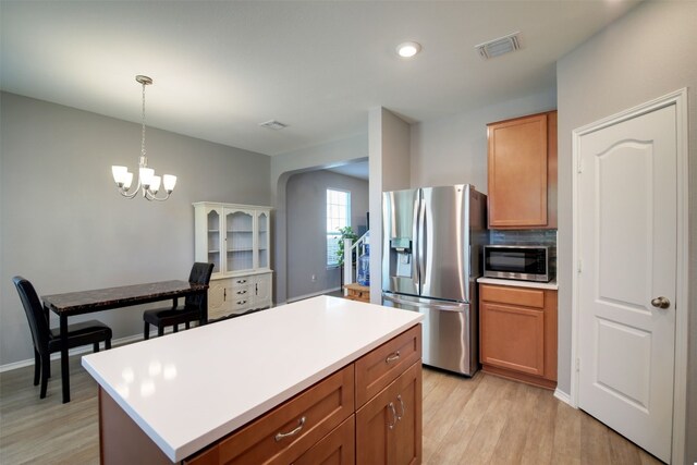 kitchen with pendant lighting, stainless steel appliances, tasteful backsplash, a kitchen island, and light wood-type flooring