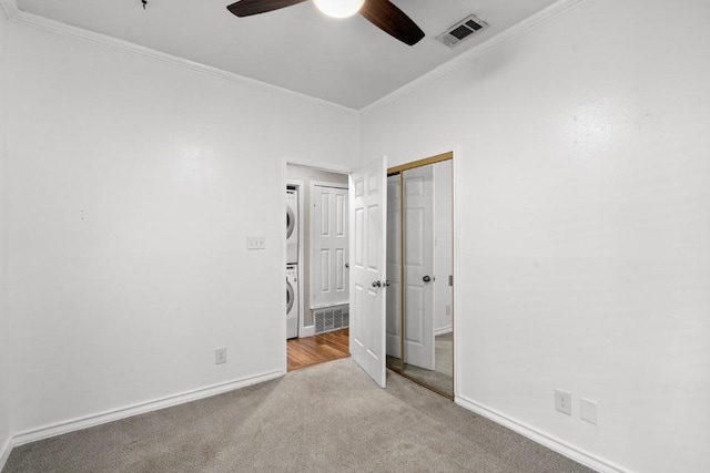 spare room featuring ceiling fan, stacked washer and dryer, light colored carpet, and ornamental molding