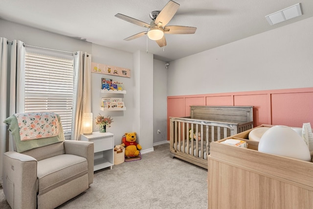 bedroom with a crib, ceiling fan, and light colored carpet