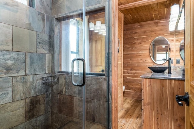 bathroom with a shower with shower door, vanity, wood ceiling, and wooden walls