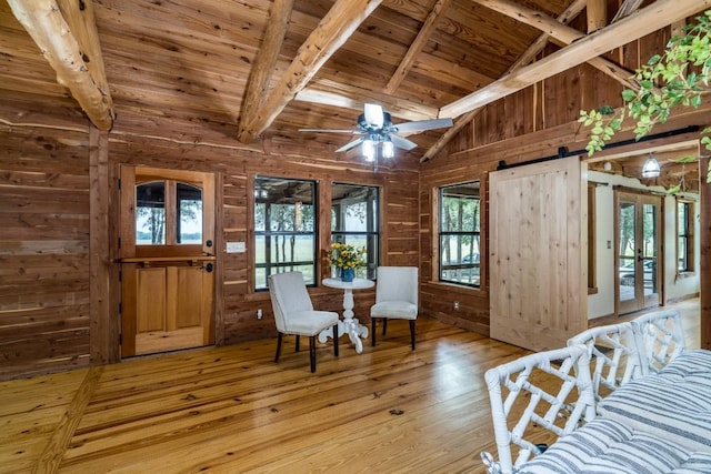 sitting room featuring lofted ceiling with beams, wooden walls, a barn door, light wood-type flooring, and wood ceiling