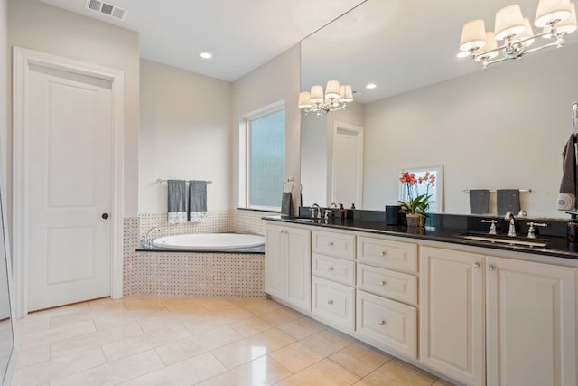 bathroom with tile patterned flooring, vanity, a relaxing tiled tub, and a notable chandelier