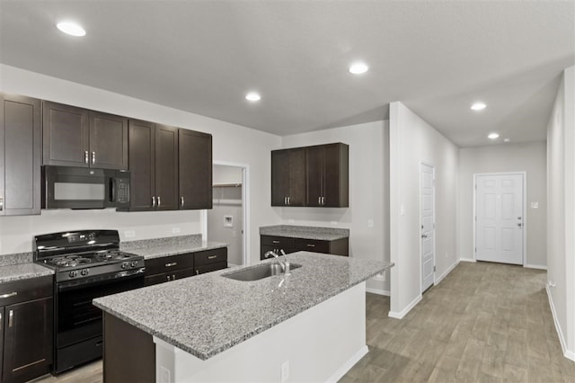 kitchen with a center island with sink, light stone counters, black appliances, sink, and light hardwood / wood-style flooring