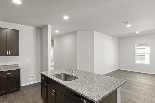 kitchen with dark wood-type flooring, a center island with sink, black dishwasher, sink, and light stone countertops