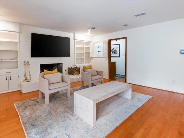 living room featuring built in shelves, light hardwood / wood-style floors, and a brick fireplace