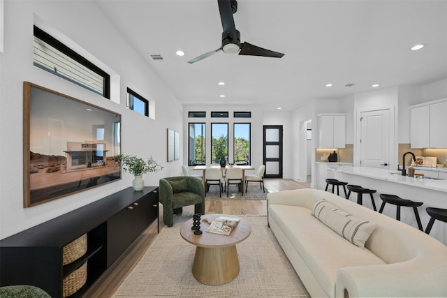 living room featuring ceiling fan, sink, and light wood-type flooring