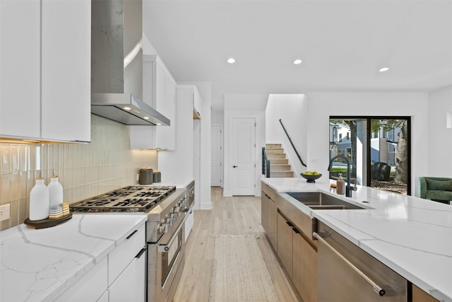 kitchen featuring white cabinets, stainless steel appliances, light stone counters, and wall chimney exhaust hood