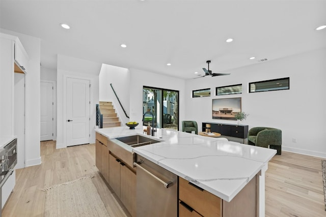 kitchen featuring light stone countertops, light wood-type flooring, stainless steel dishwasher, a kitchen island with sink, and ceiling fan