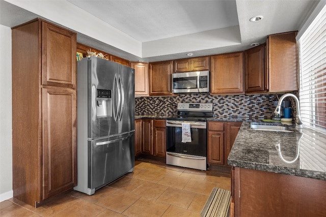 kitchen featuring sink, decorative backsplash, dark stone countertops, light tile patterned floors, and appliances with stainless steel finishes