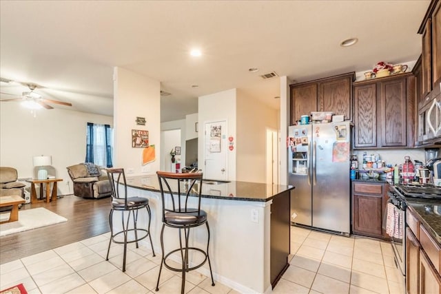 kitchen with ceiling fan, a center island, dark stone countertops, light tile patterned floors, and appliances with stainless steel finishes