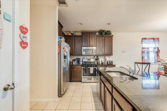 kitchen with dark stone counters, sink, appliances with stainless steel finishes, tasteful backsplash, and light tile patterned flooring