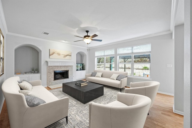 living room with ceiling fan, built in features, light wood-type flooring, and ornamental molding