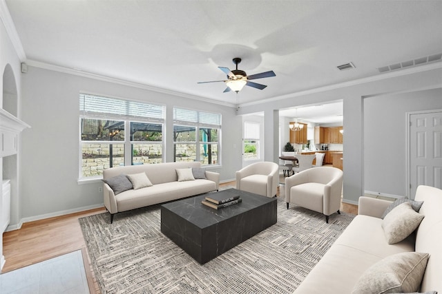 living room with ceiling fan with notable chandelier, light hardwood / wood-style floors, a wealth of natural light, and ornamental molding