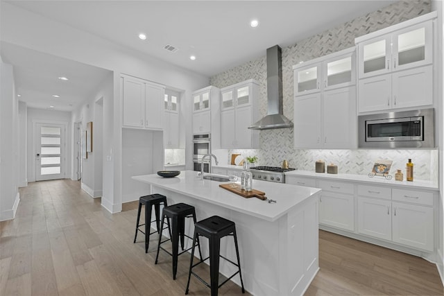 kitchen featuring white cabinetry, an island with sink, wall chimney exhaust hood, and stainless steel appliances