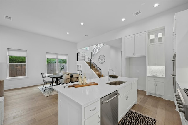 kitchen with a center island with sink, white cabinets, sink, light wood-type flooring, and appliances with stainless steel finishes