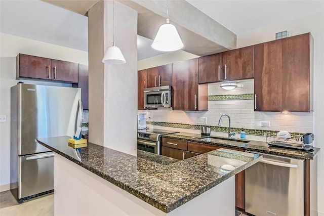 kitchen featuring appliances with stainless steel finishes, decorative light fixtures, a sink, and dark stone countertops