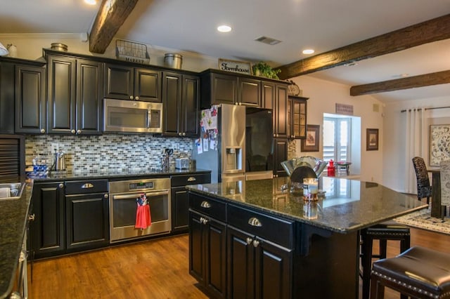 kitchen featuring a center island, beamed ceiling, light hardwood / wood-style floors, a kitchen bar, and appliances with stainless steel finishes