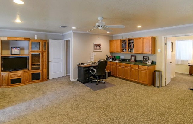 carpeted office space with ceiling fan, built in desk, and crown molding