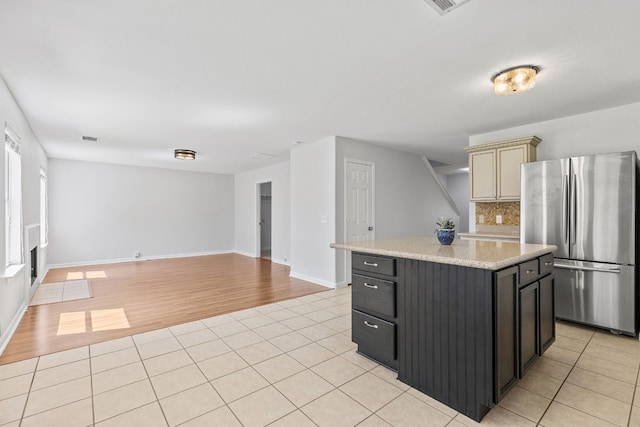 kitchen featuring stainless steel fridge, tasteful backsplash, light tile patterned floors, cream cabinetry, and a center island