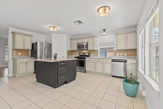 kitchen featuring sink, stainless steel appliances, a kitchen island, cream cabinets, and light tile patterned flooring