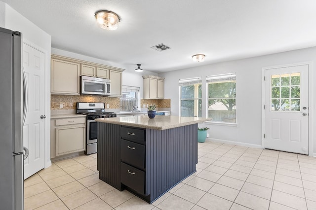 kitchen with cream cabinets, light tile patterned floors, tasteful backsplash, a kitchen island, and stainless steel appliances