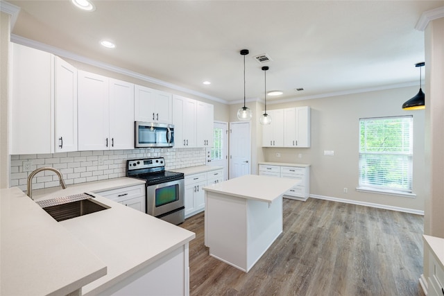 kitchen with appliances with stainless steel finishes, a center island, light countertops, white cabinetry, and a sink