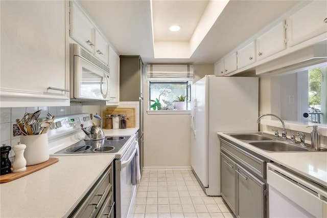 kitchen with white cabinets, white appliances, a tray ceiling, and sink