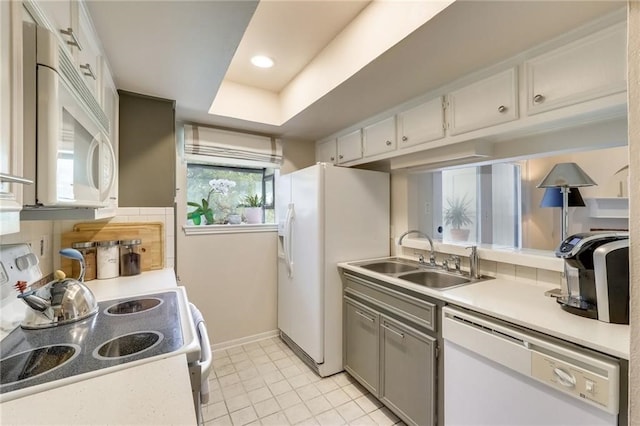 kitchen with white appliances, sink, light tile patterned floors, a tray ceiling, and white cabinetry